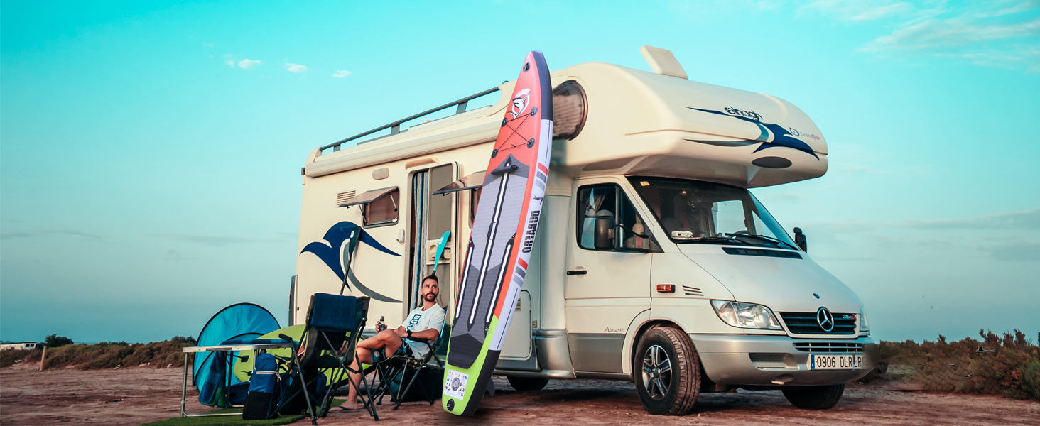 Camping-car blanc garé dans un décor désertique avec des planches de surf, des chaises de camping et d'autres équipements de plein air visibles