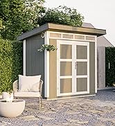 Terrasse extérieure avec cabanon moderne, chaises blanches et jardinières décoratives. Un trottoir en pierre et une végétation luxuriante entourent l'espace. Feuilles d'automne visibles sur les arbres.