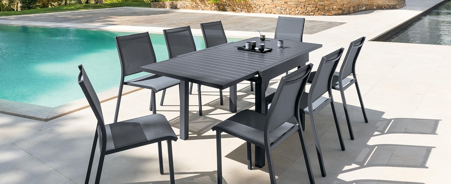 avec table rectangulaire en métal gris et huit chaises assorties, placé sur un patio au bord d'une piscine dans un jardin luxuriant.
