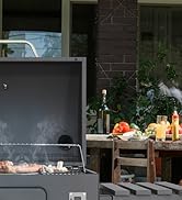 Installation d'un barbecue extérieur avec surface de cuisson carbonisée, exposée sur la terrasse avec table, légumes et scène divertissante en plein air en soirée.